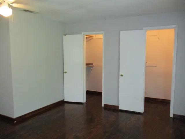 Room featuring dark wood-finish flooring, light gray walls, white trim, and two open closets with shelving
