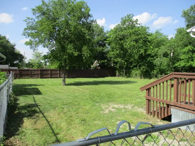 Expansive grassy yard featuring a wood privacy fence, mature trees, a chain-link fence, and a wooden deck with stairs