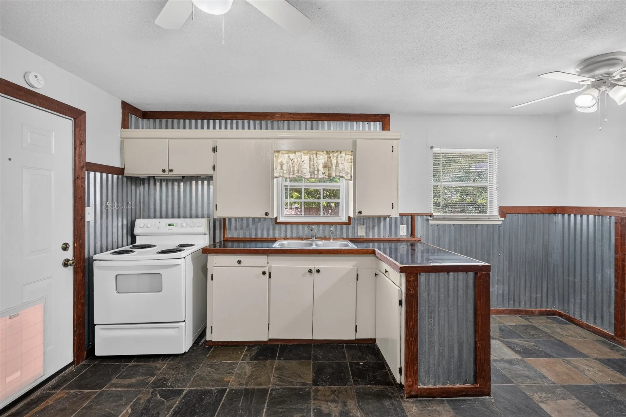Kitchen featuring white cabinetry, a built-in double basin sink, dark countertops, and corrugated metal wainscoting
