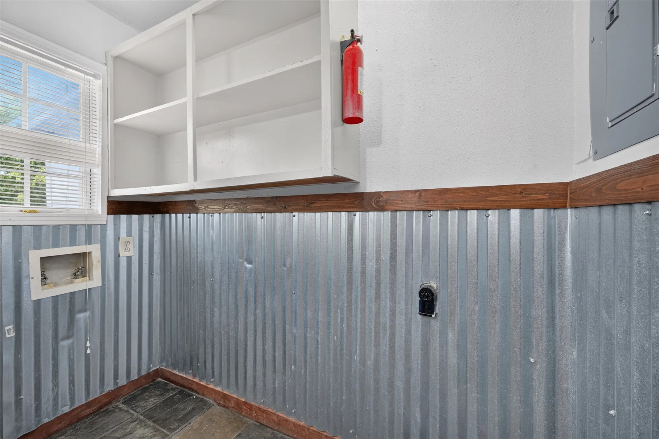 Built-in overhead shelving, corrugated metal wainscoting, wood-finish trim, window with blinds, and slate tile flooring