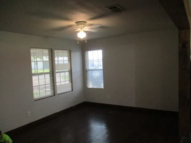 Spacious room featuring dark wood-finish flooring, multiple windows, and a ceiling fan with integrated lighting