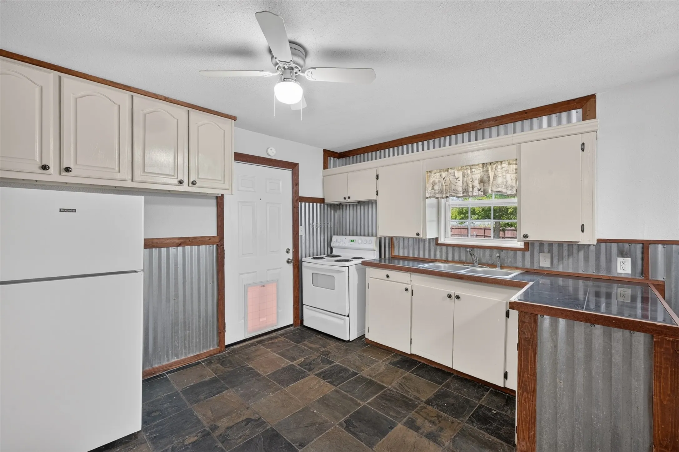 Kitchen featuring white cabinetry, a dual-basin stainless steel sink, checkerboard floor tiles, and a ceiling fan with integrated lighting