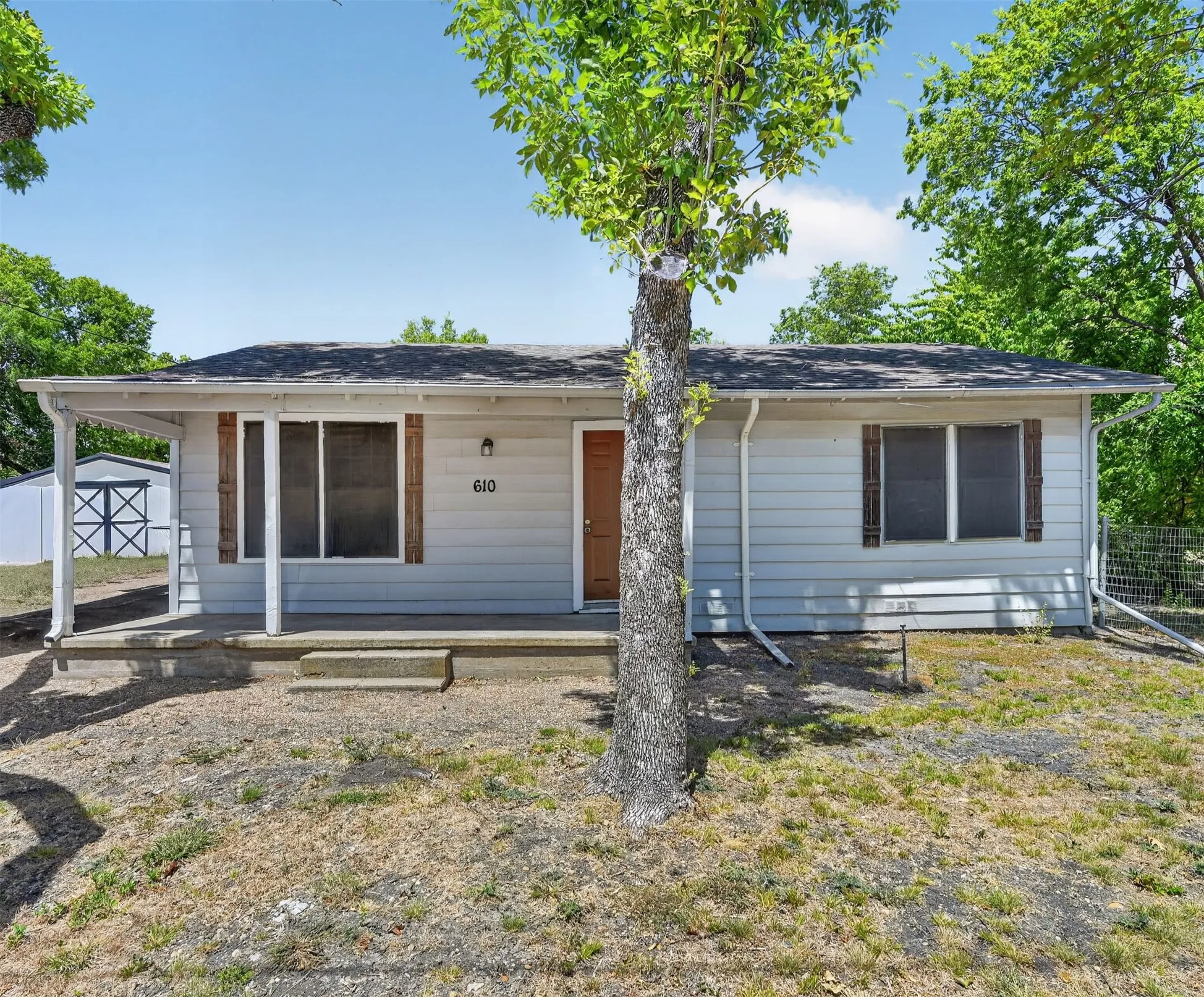 Light-colored siding exterior with a covered porch, wood-look window shutters, and a front entry door