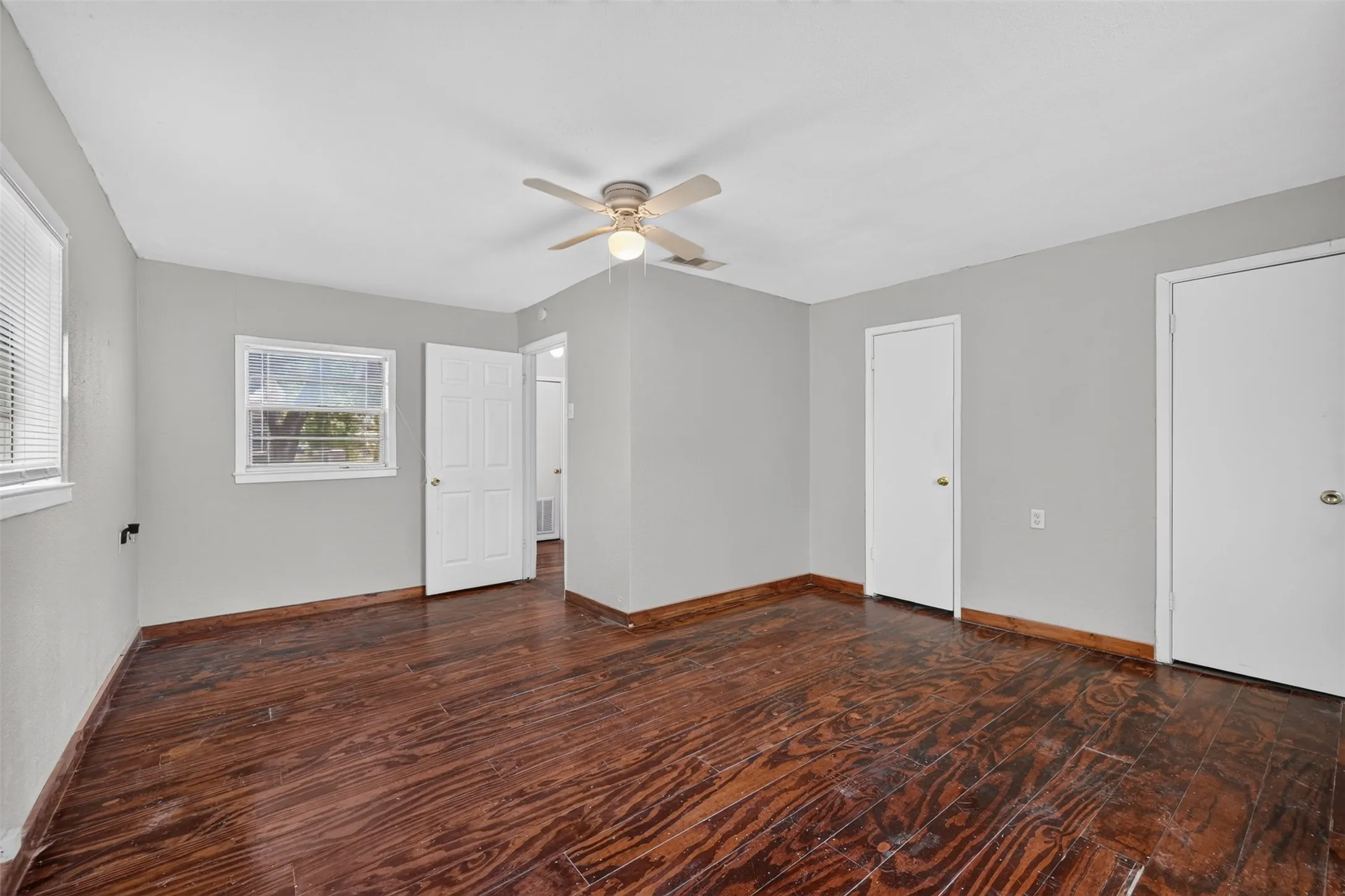 Dark wood-finish flooring with light gray walls, white trim, and a ceiling fan with integrated lighting