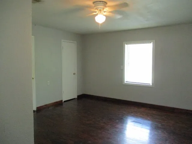 Spacious interior room featuring wood-finish flooring, a single window, and a ceiling fan with integrated lighting