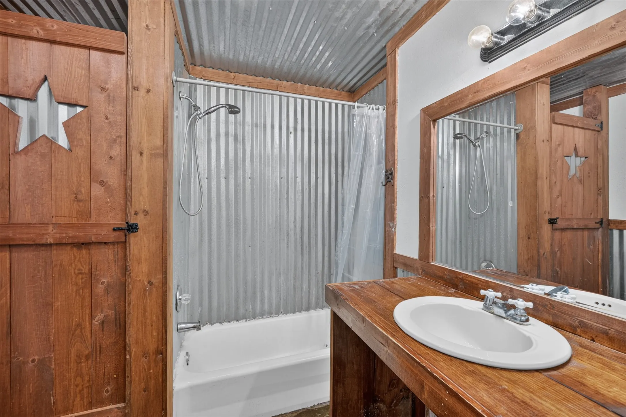 Corrugated metal shower surround, wood-finish vanity with an undermount sink, and a framed mirror
