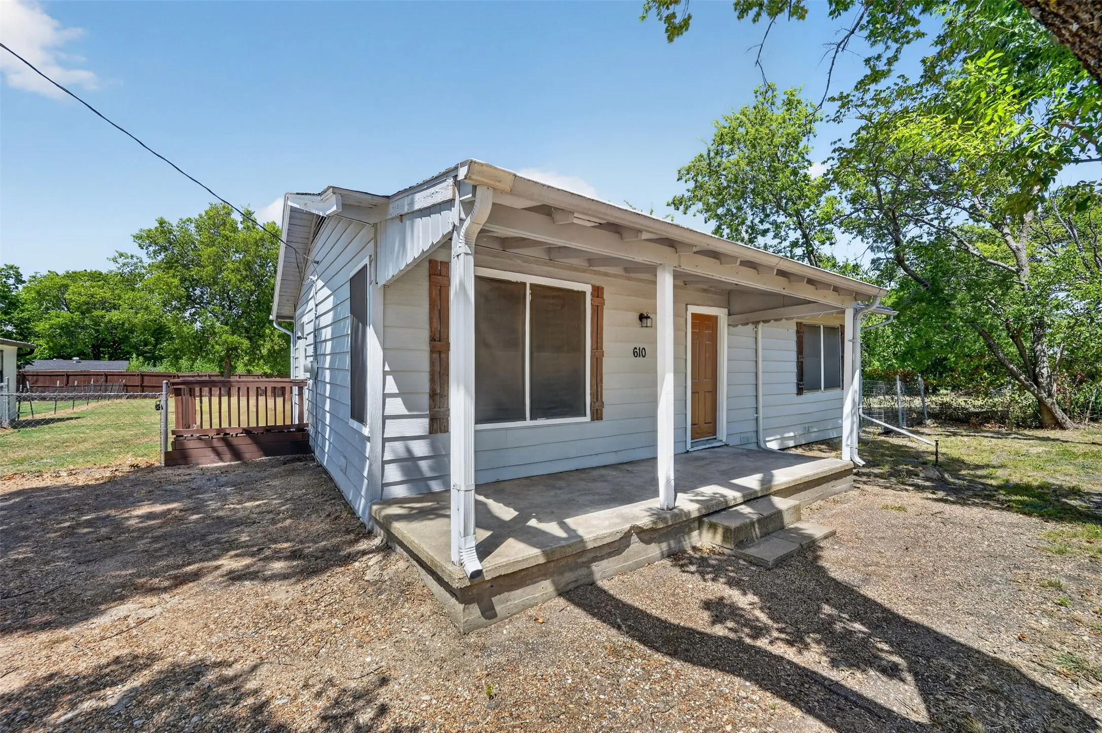 Covered concrete front porch with steps, light blue siding, and a wood-tone entry door
