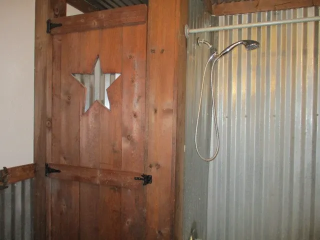 Wood-paneled interior door with a star cut-out detail, complemented by corrugated metal wall panels and a mounted shower fixture