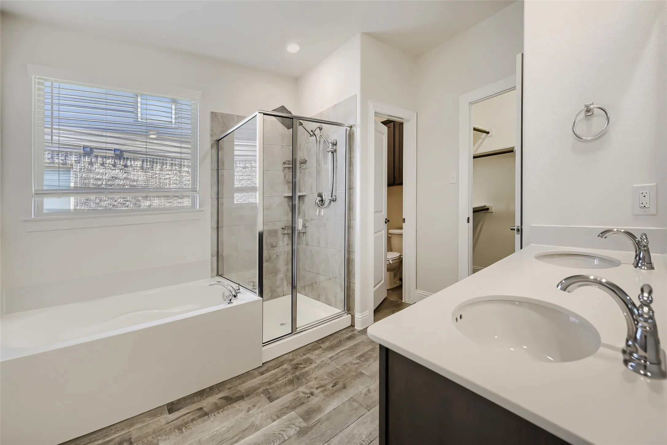Bathroom featuring a dual vanity with undermount sinks, a walk-in shower with glass enclosure, a separate soaking tub, and wood-finish flooring