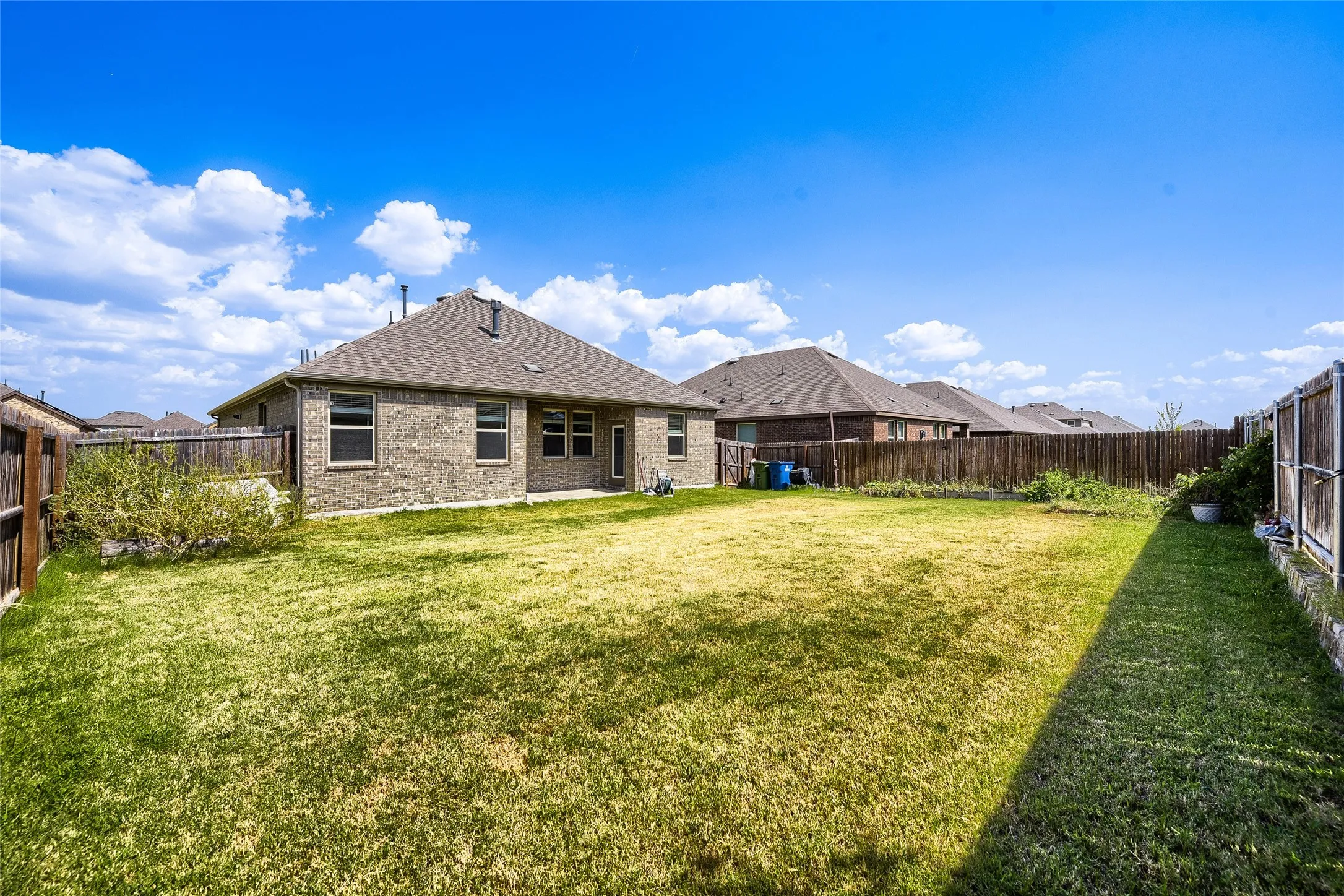 Expansive backyard featuring a large green space, privacy fencing, and a brick exterior