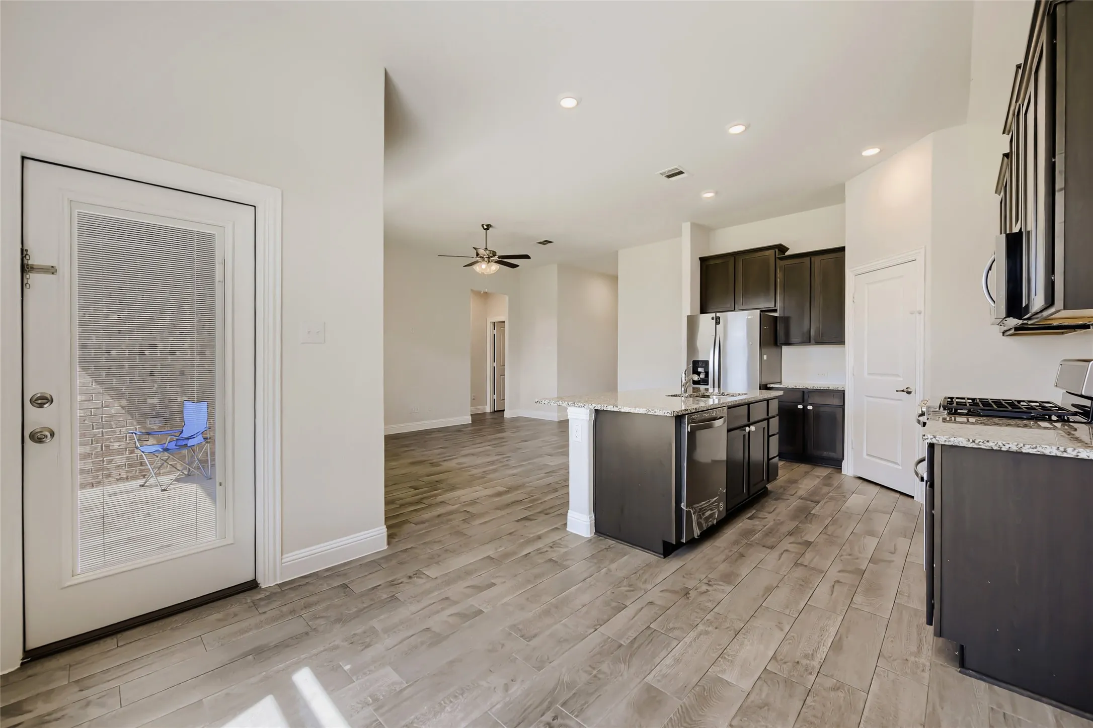 Open-concept kitchen featuring an island with stone countertop, dark wood cabinetry, stainless steel appliances, and wood-finish flooring