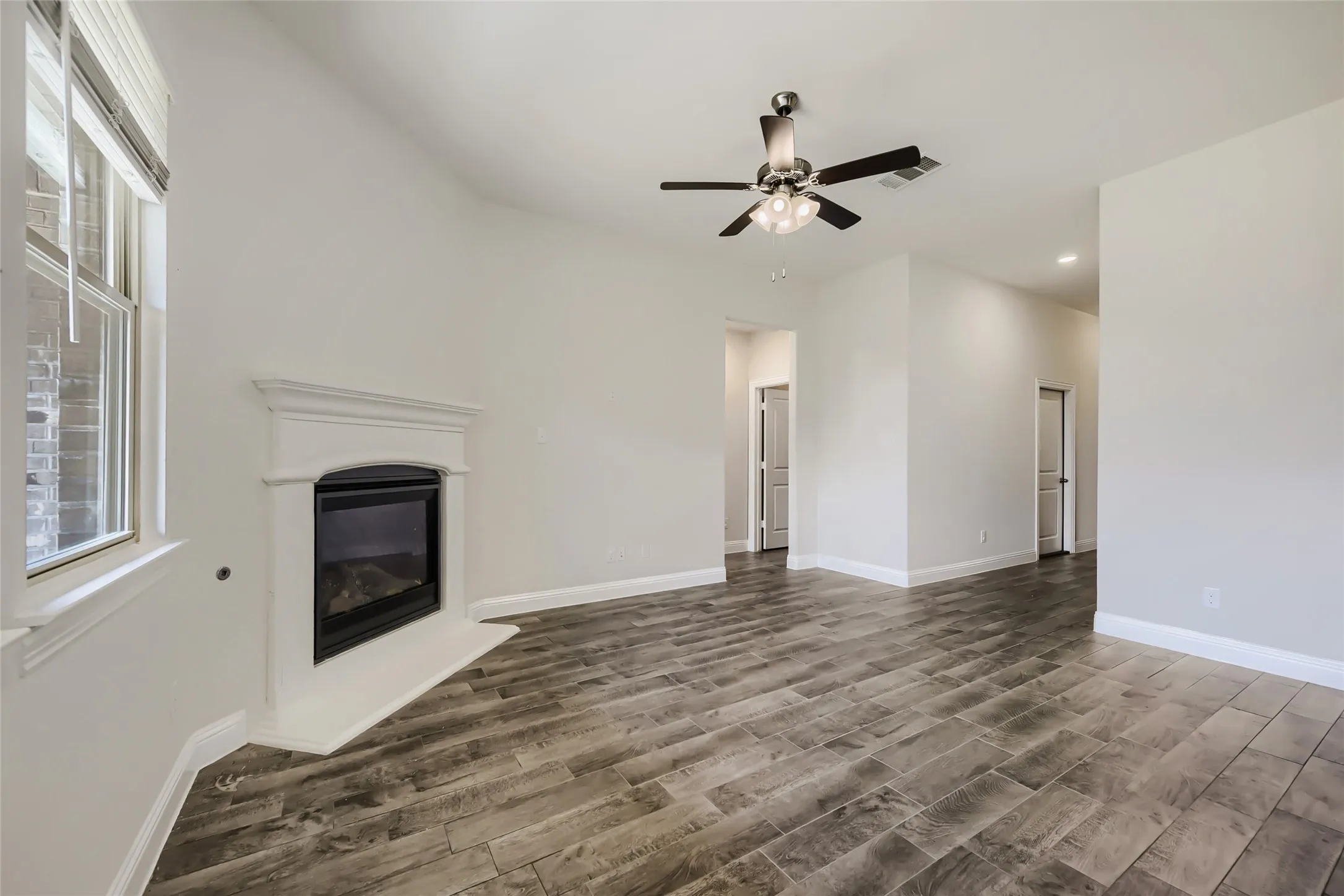 Spacious interior with wood-finish flooring, a contemporary fireplace, and a ceiling fan with integrated lighting