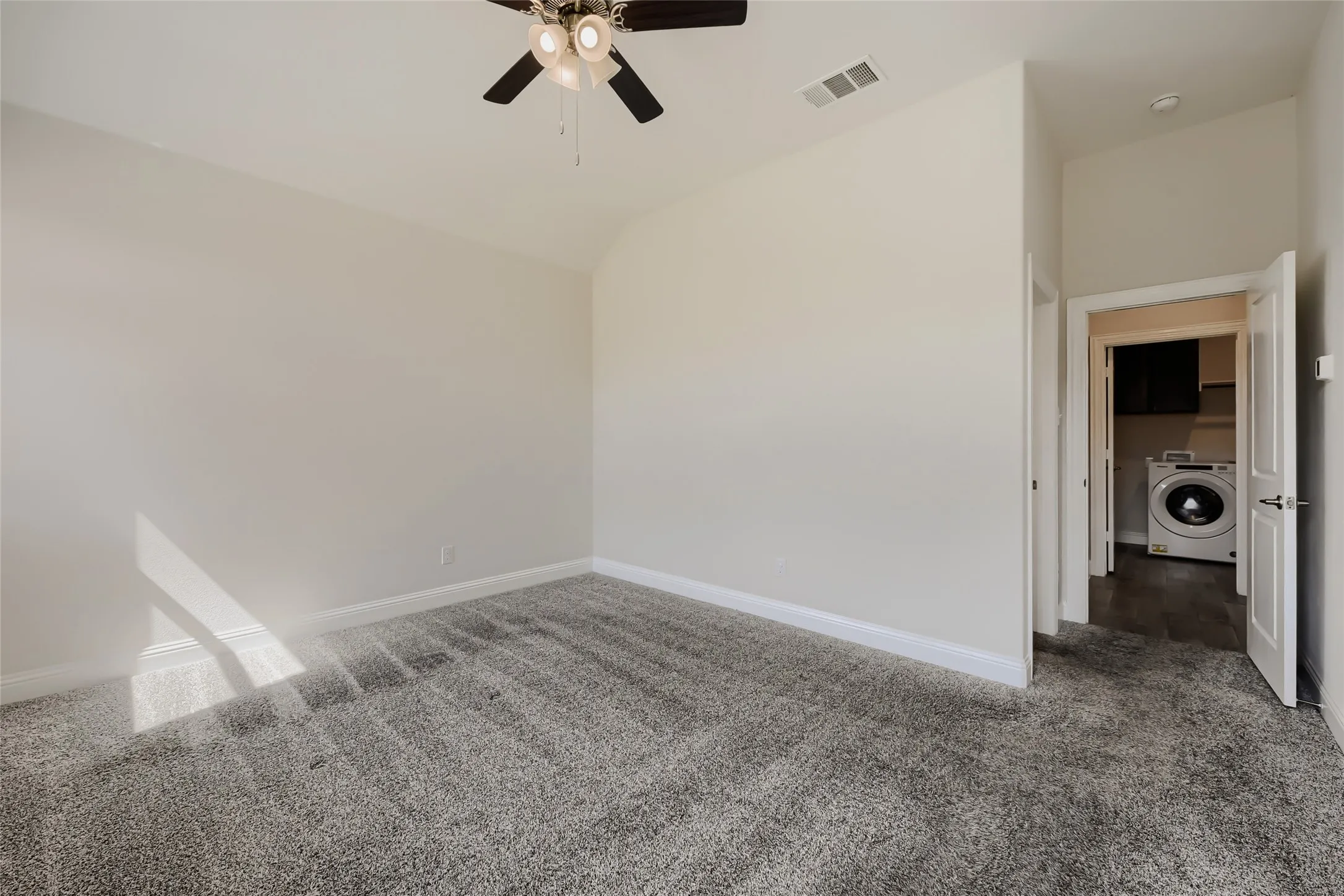 Carpeted room with a ceiling fan featuring a laundry area visible through an open doorway
