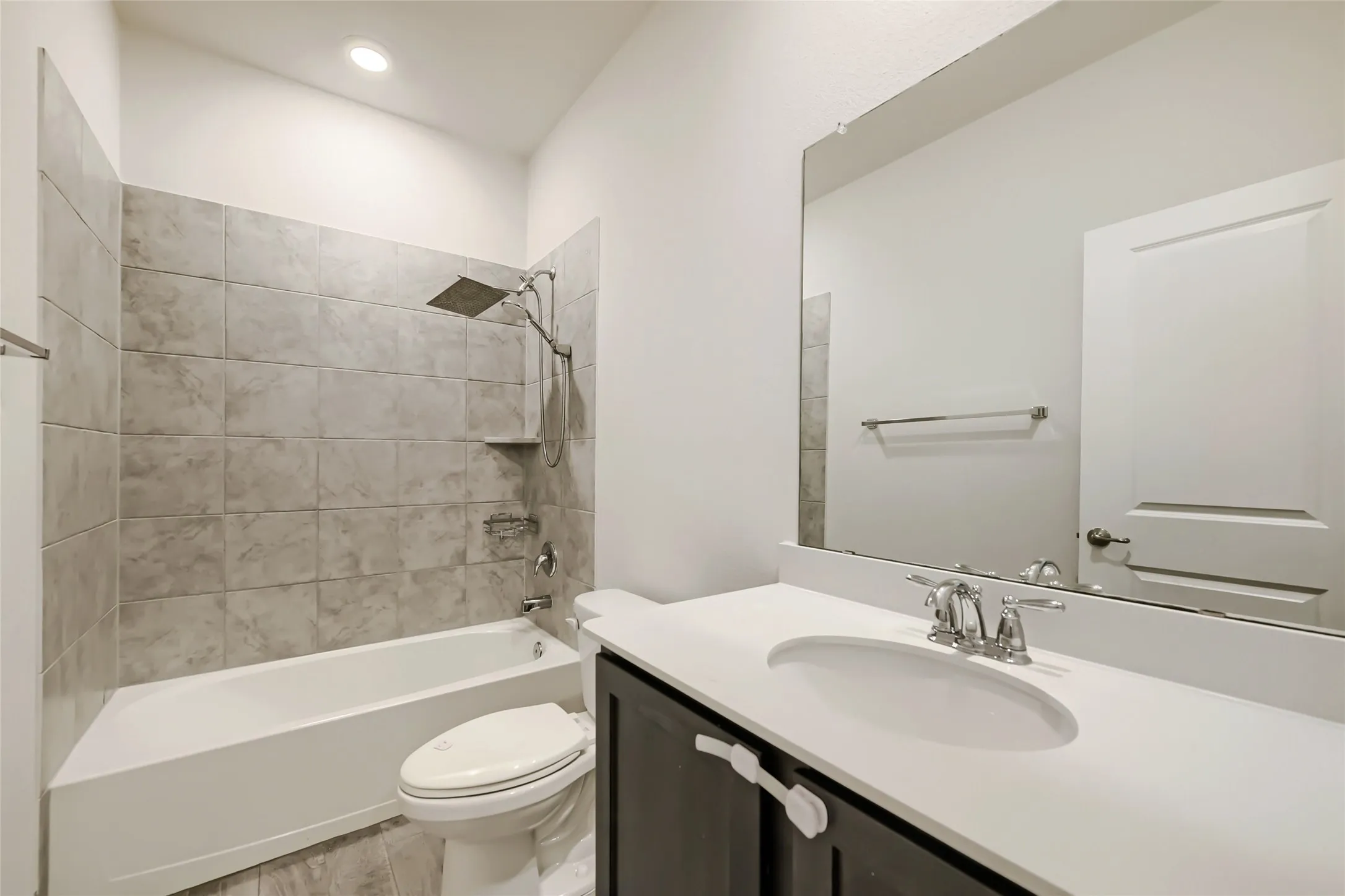 Bathroom featuring a shower/tub combination with light grey tile surround, a built-in shelf, and a rain shower head