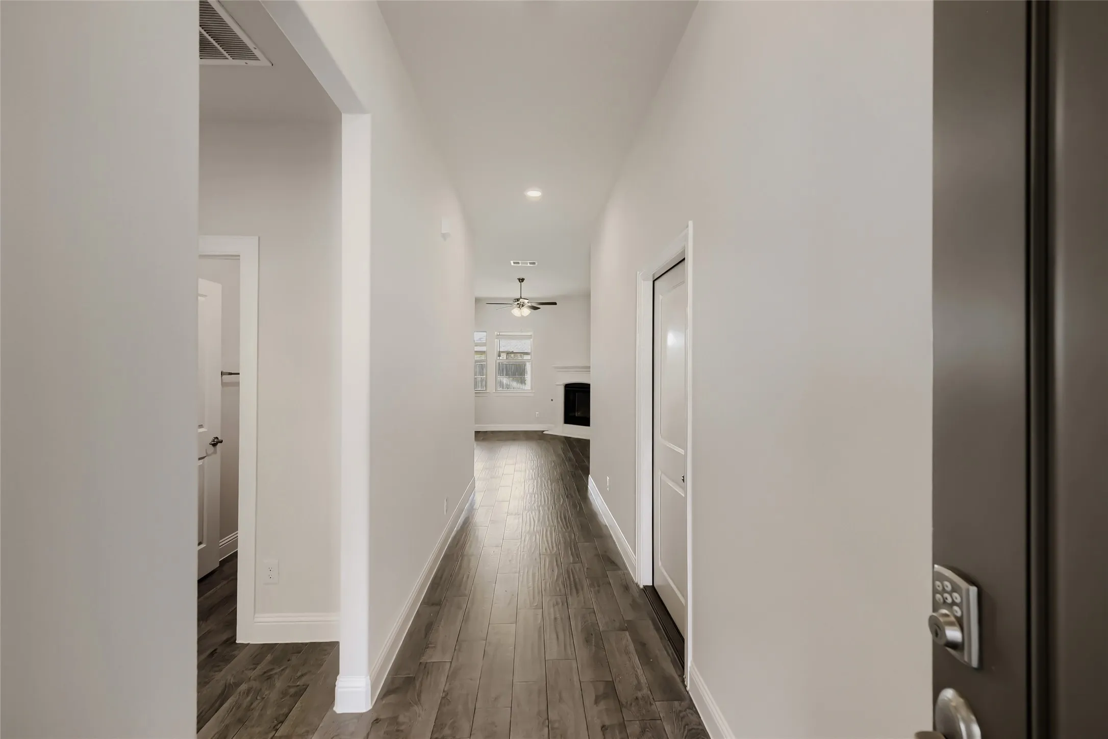 Long hallway with wood-finish flooring, white baseboards, and light neutral wall paint