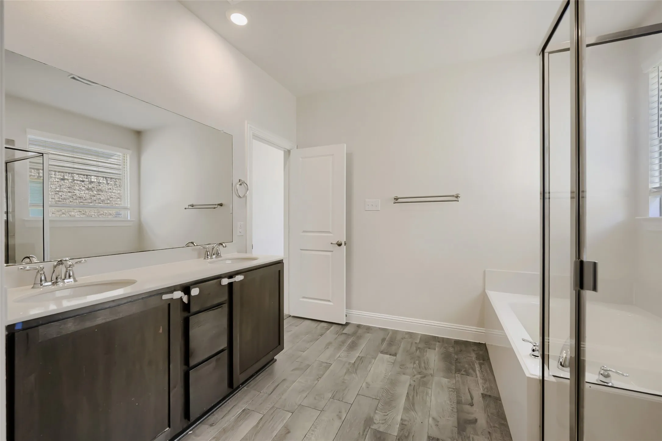 Spacious bathroom featuring a dual vanity with dark wood-finish cabinetry, a large frameless mirror, and a built-in tub with a glass-enclosed shower