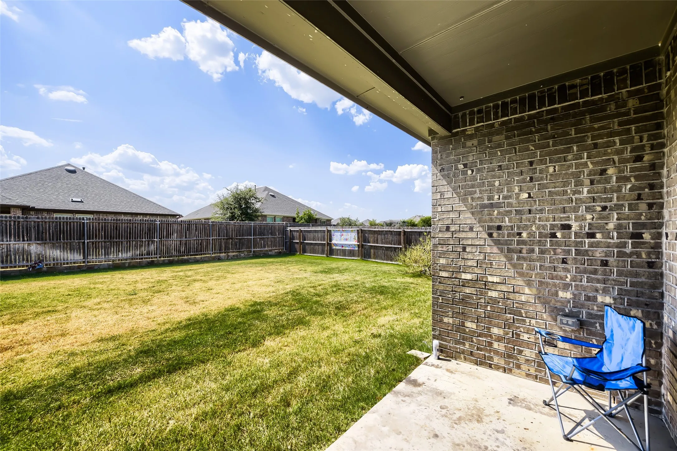 Expansive backyard with a manicured lawn, full privacy fencing, and a concrete patio