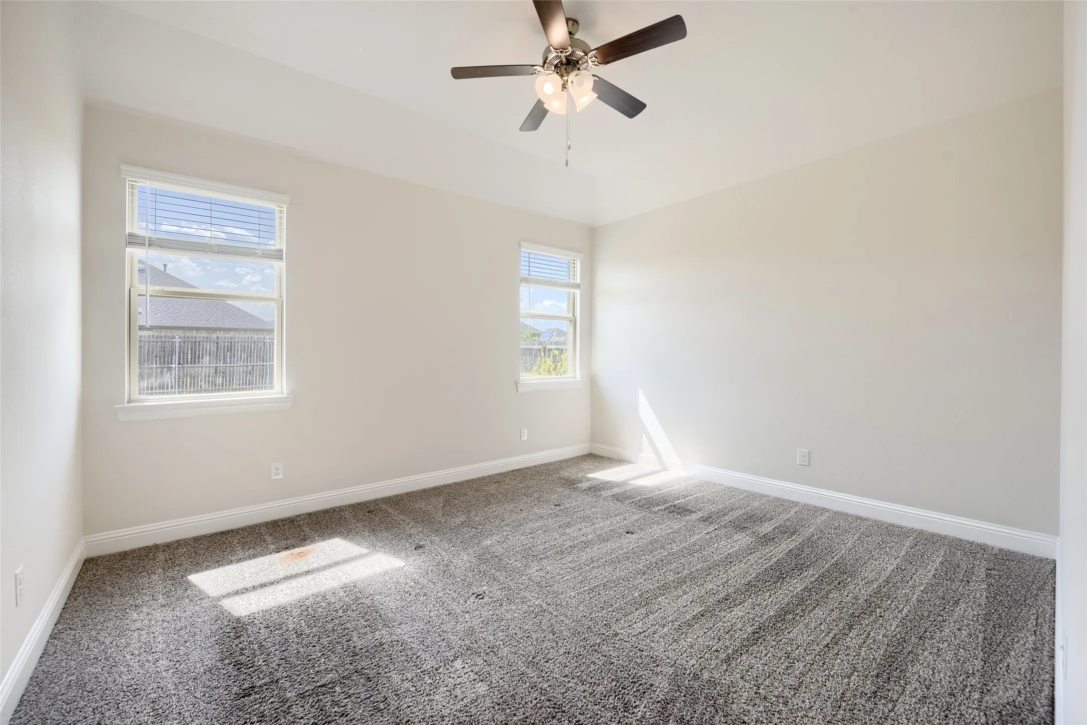 Spacious room featuring neutral carpeting, light-colored walls, and a ceiling fan with integrated lighting