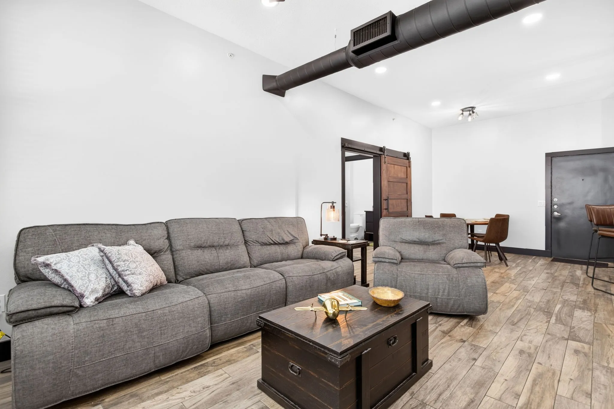 Spacious living area featuring wood-finish flooring, exposed ductwork, recessed lighting, and a barn door entry