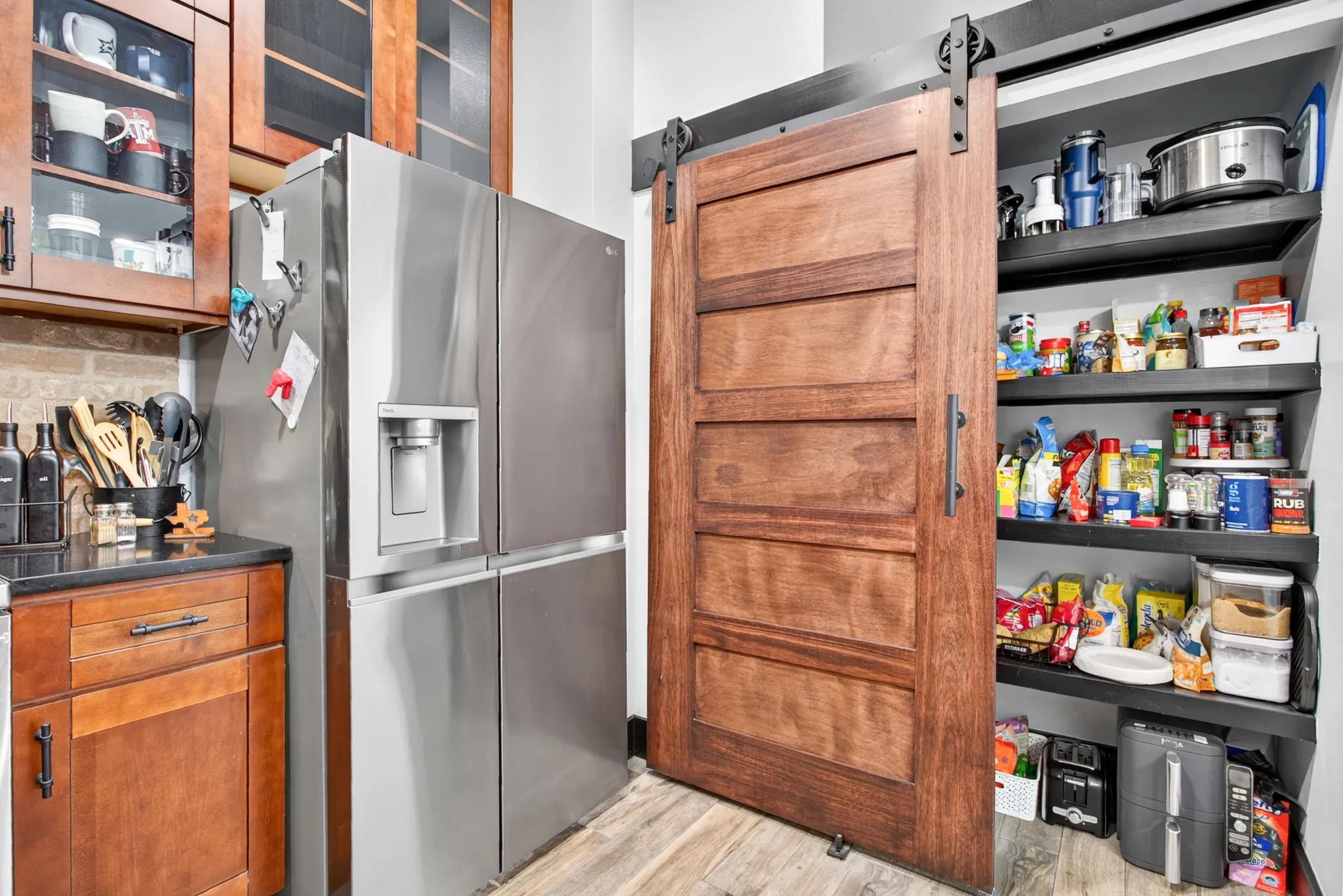 Kitchen pantry featuring a sliding barn door with dark hardware, built-in shelving, wood-finish flooring, and a stone countertop