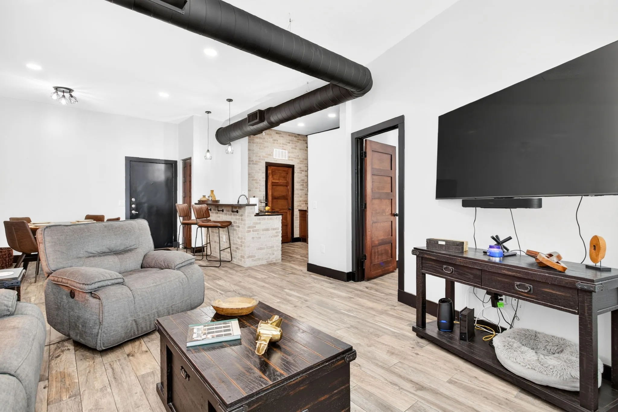 Spacious open-concept interior featuring light wood-finish flooring, exposed black ductwork, and white walls