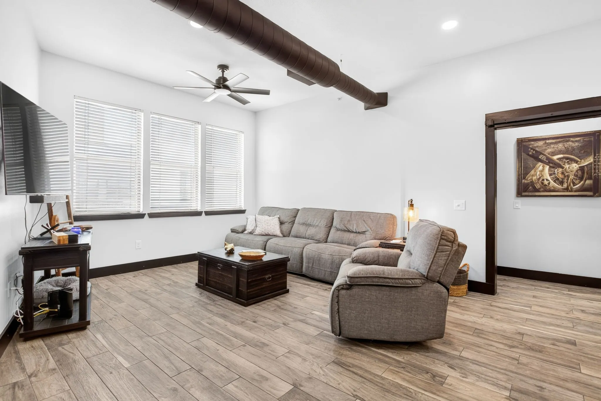 Open concept living area featuring wood-finish flooring, high ceilings, a ceiling fan, and exposed industrial-style ductwork