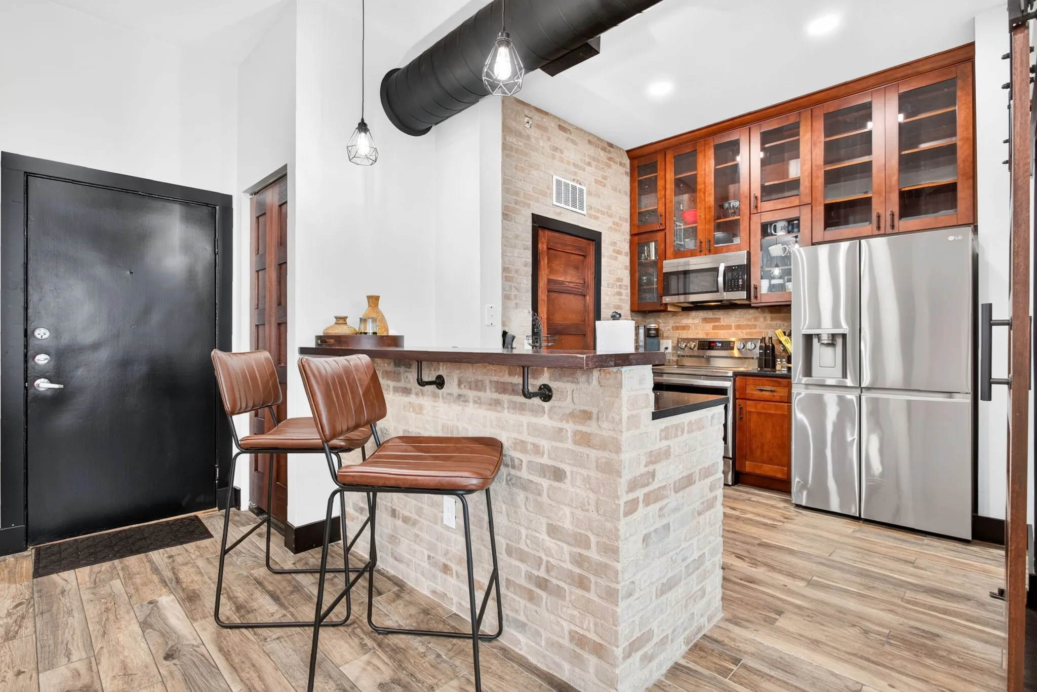 Kitchen area featuring brick-style detailing on the island, stainless steel appliances, wood-finish flooring, recessed lighting, and exposed ductwork