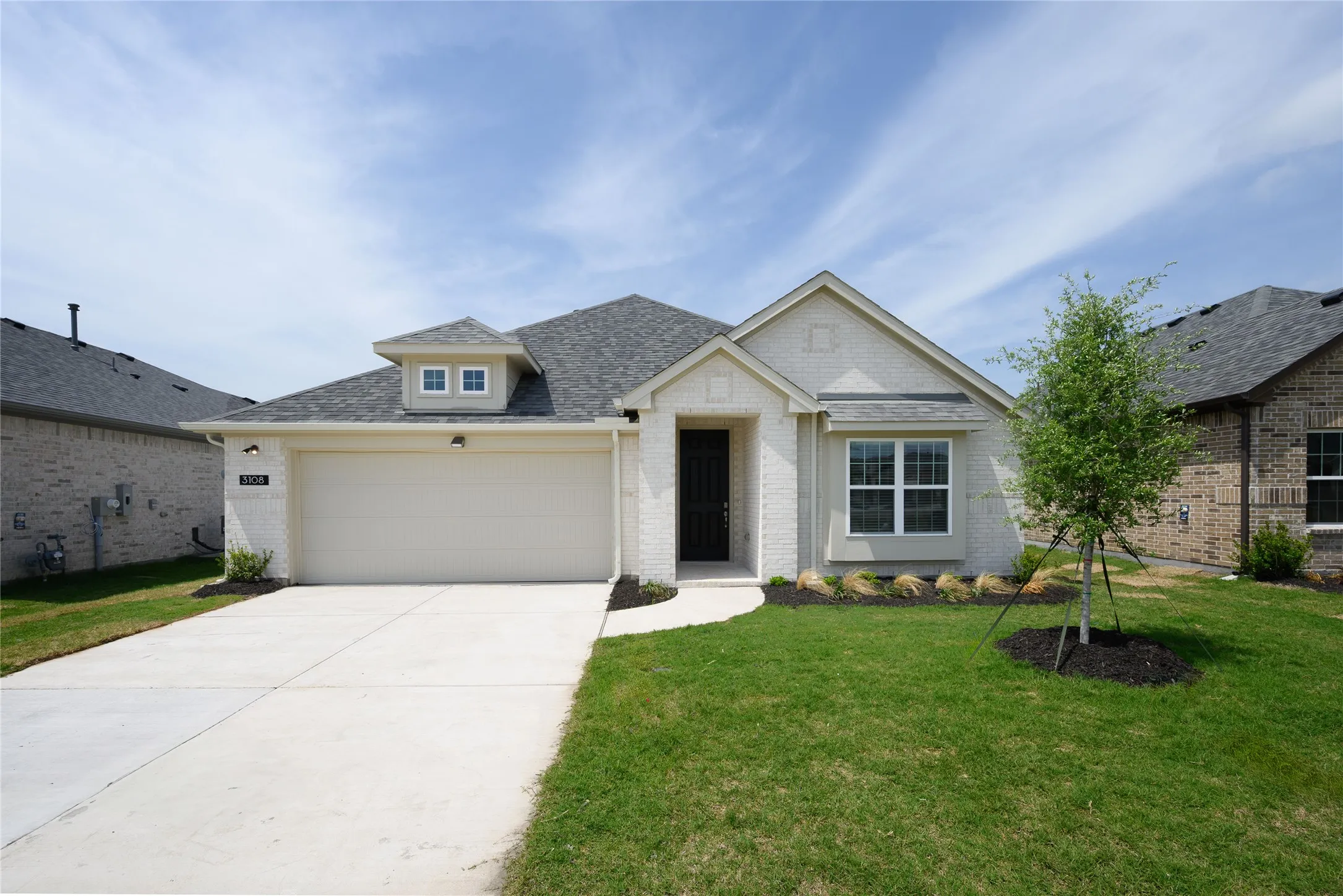 View of front of property featuring a front lawn, a garage, a shingled roof, driveway, and brick siding