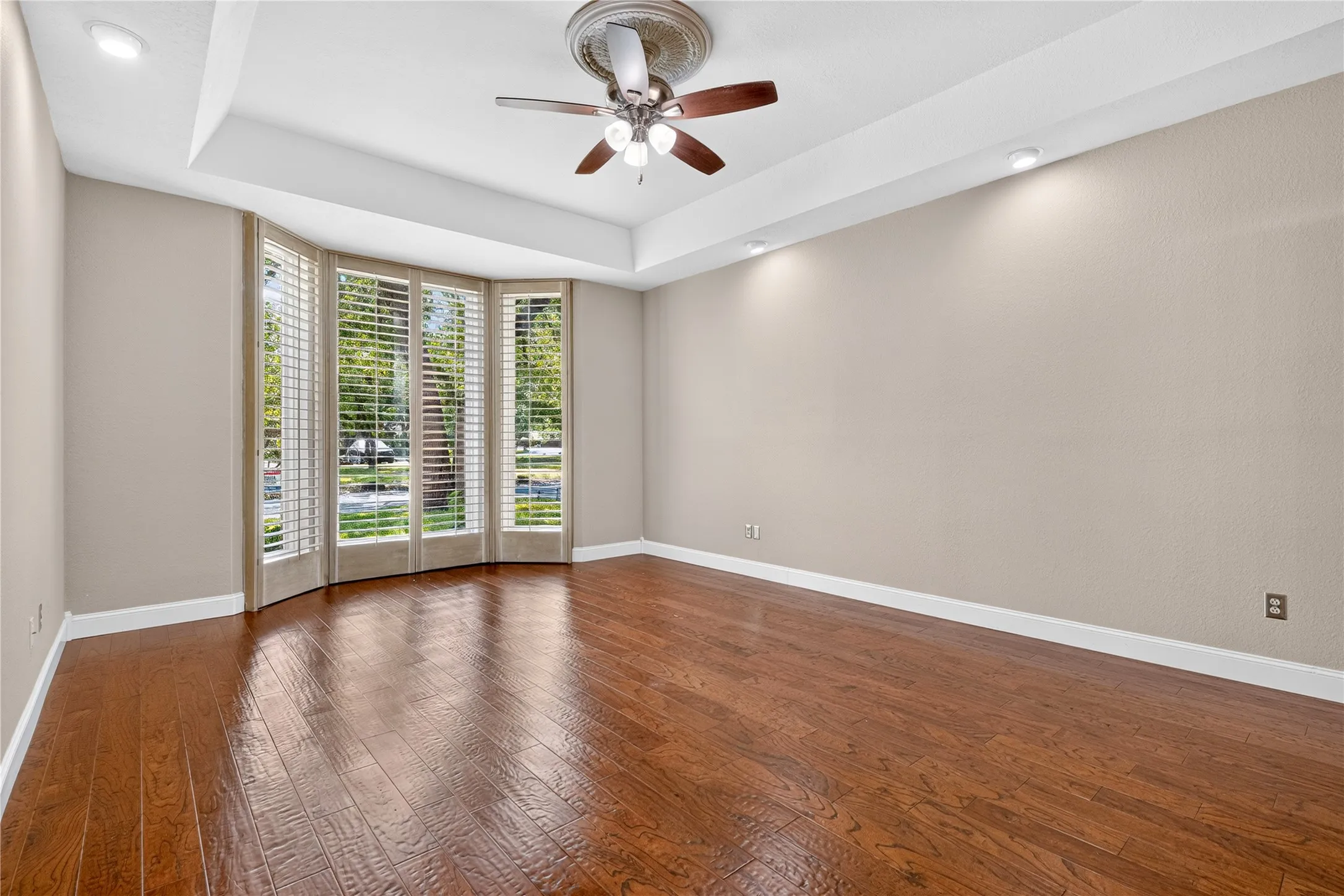 Primary suite offers a tray ceiling and floor to ceiling wood louver shutters to match formal dining and upstairs bedrooms.