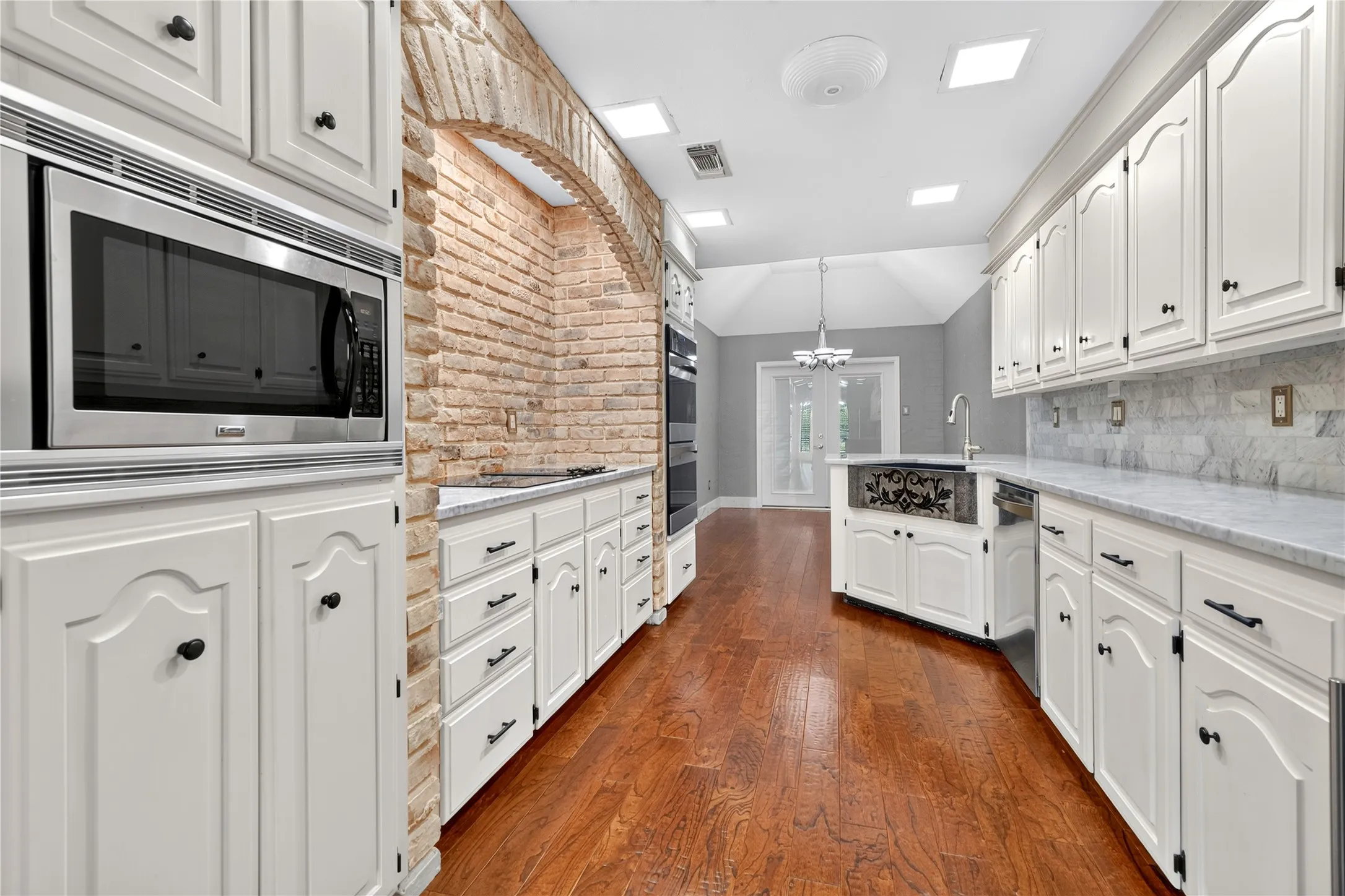 An abundance of marble counter top prep space and storage with double ovens and decorative farm sink.
