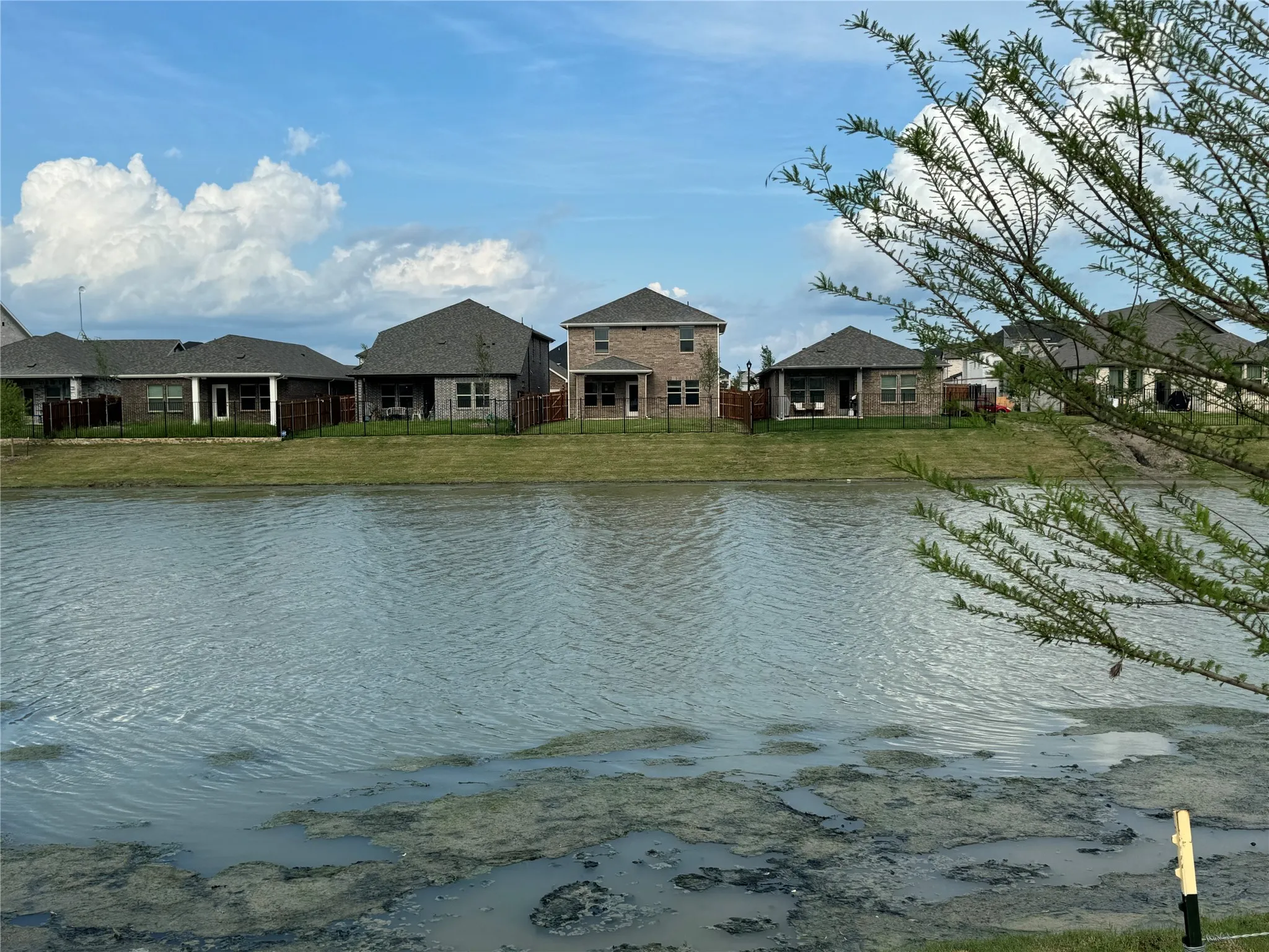 Rear exterior of a brick home with a covered patio, overlooking a body of water