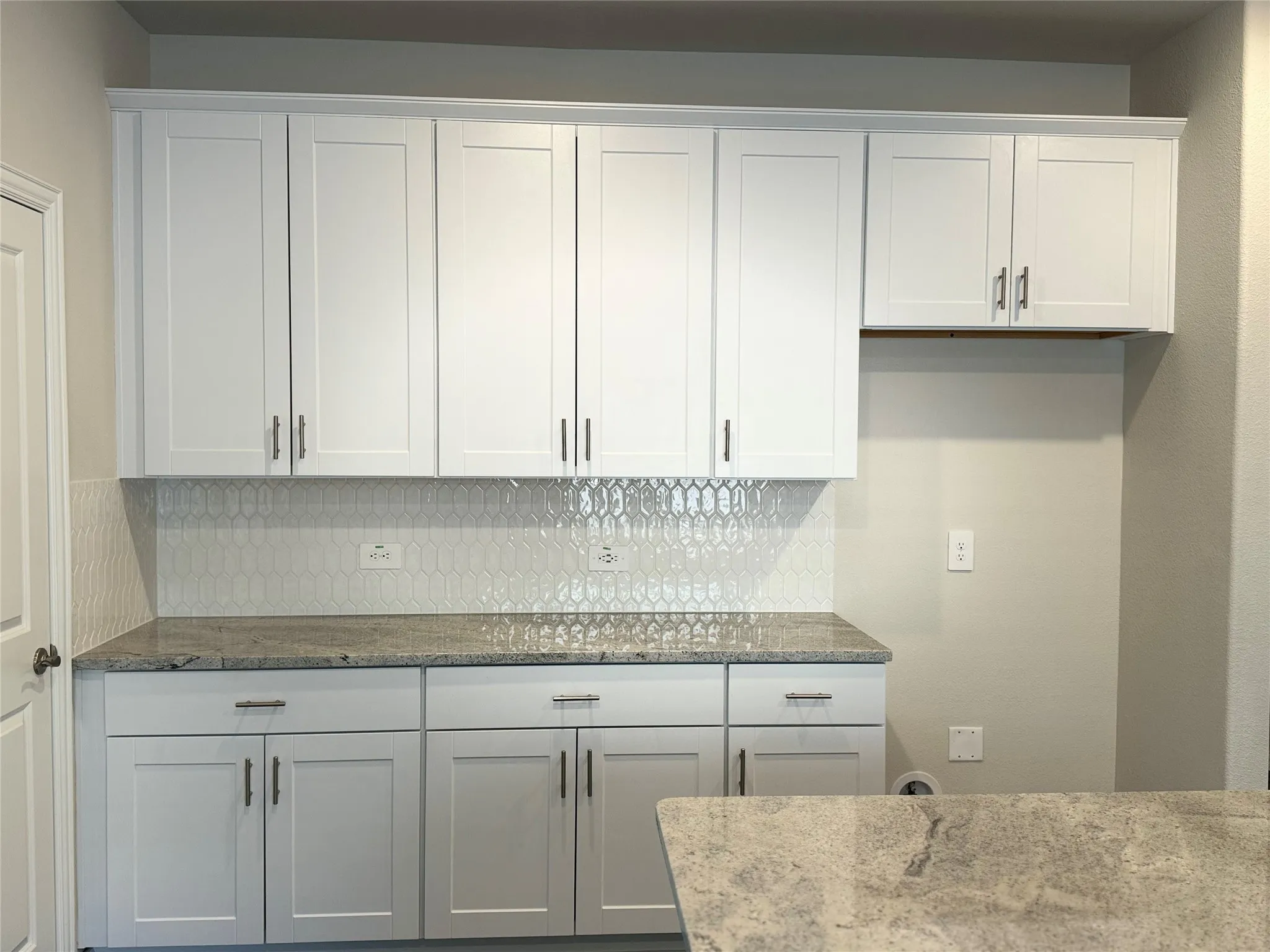 Kitchen featuring white shaker-style cabinetry, light-toned countertops, and a decorative tile backsplash