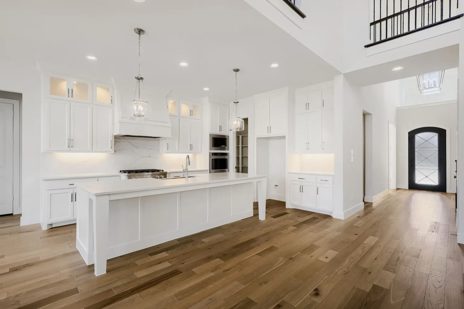 Open-concept kitchen featuring an expansive center island, white cabinetry with integrated lighting, wood-finish flooring, a built-in oven, and a gas range
