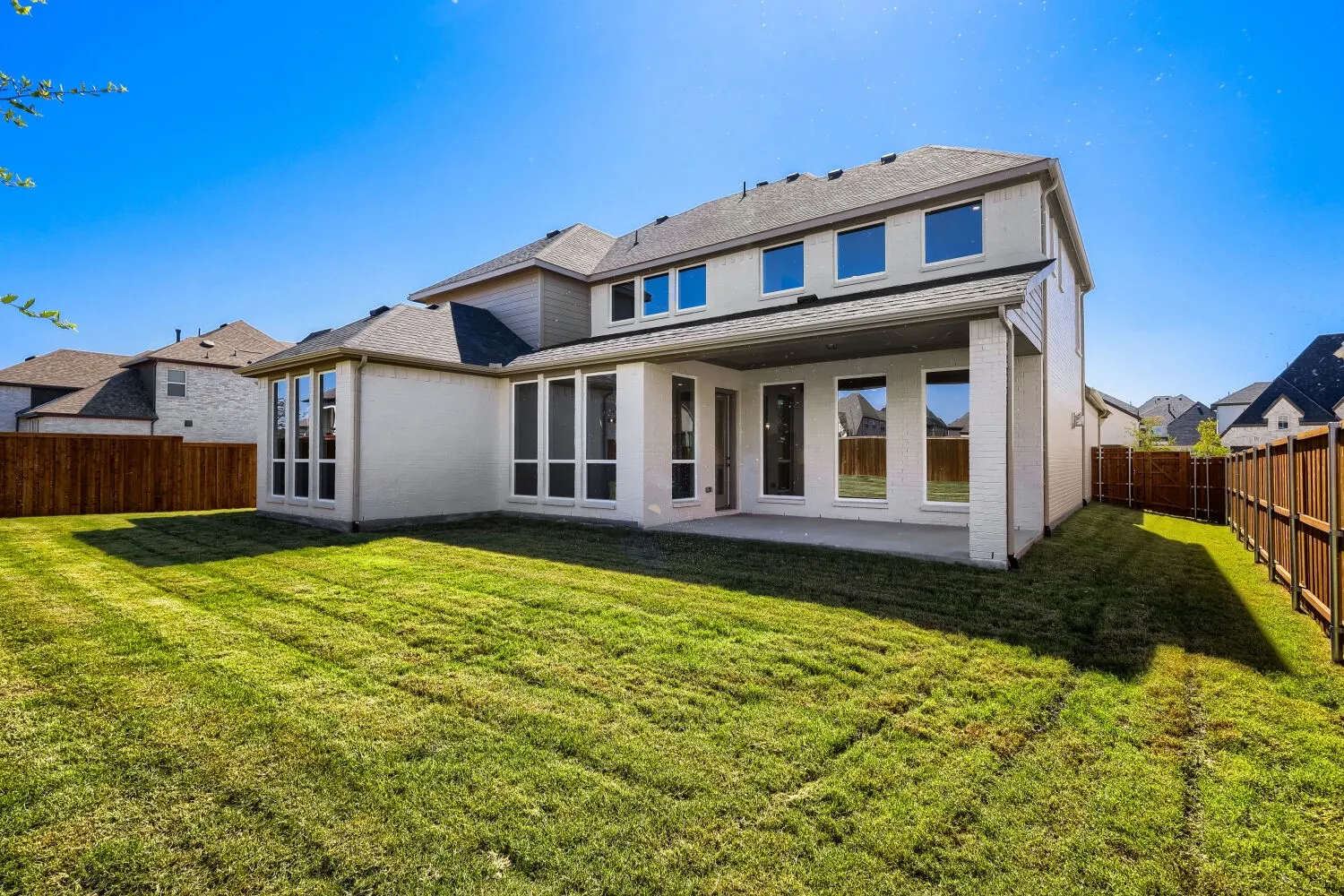 Expansive backyard featuring a manicured lawn, a covered concrete patio, multiple large windows, and a wood privacy fence