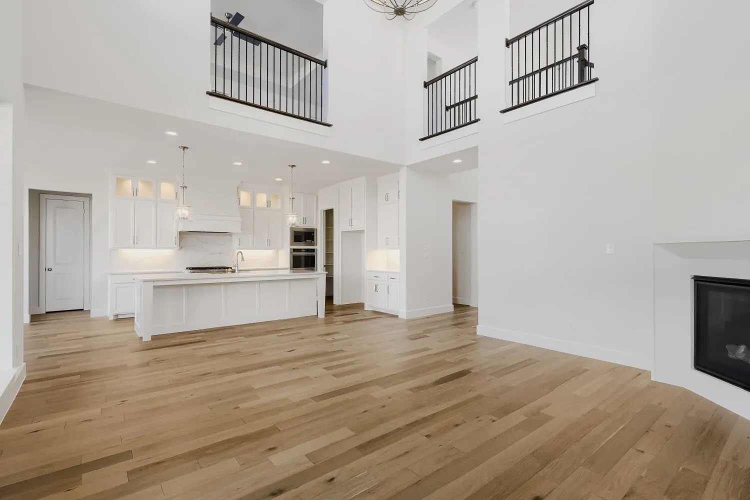 Two-story great room featuring wood-finish flooring, a built-in fireplace, and an open-concept kitchen with white cabinetry and an island