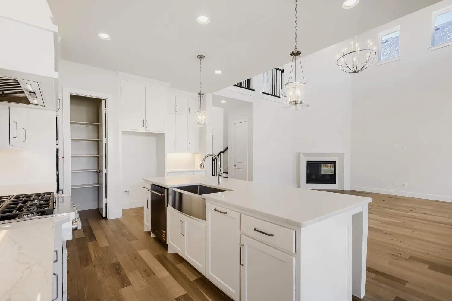 Kitchen island with a farmhouse sink and quartz countertops, white cabinetry, wood-finish flooring, a built-in gas range, and an adjacent fireplace