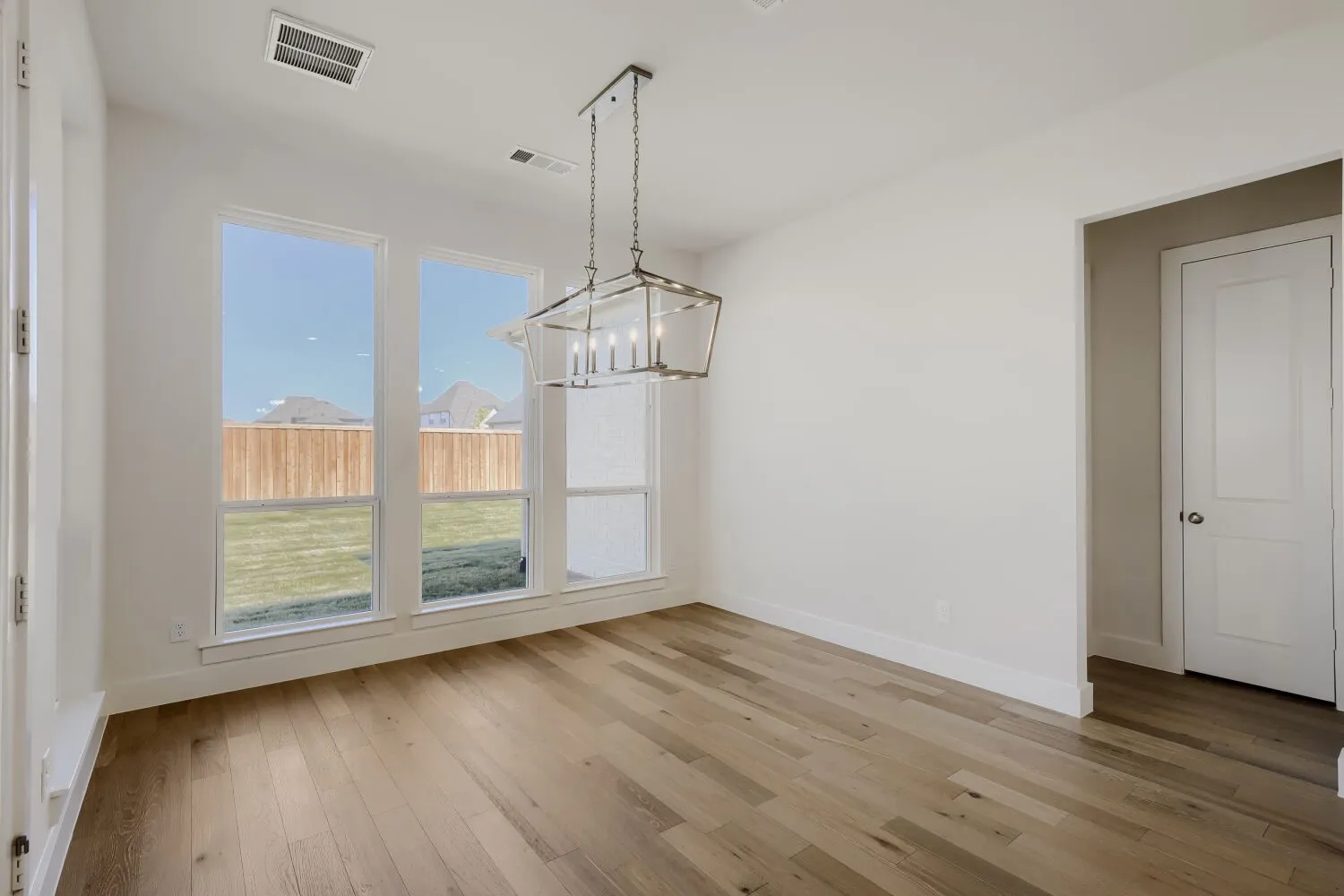 Recessed light fixture, wood-finish flooring, multiple windows, white interior door, and a modern chandelier