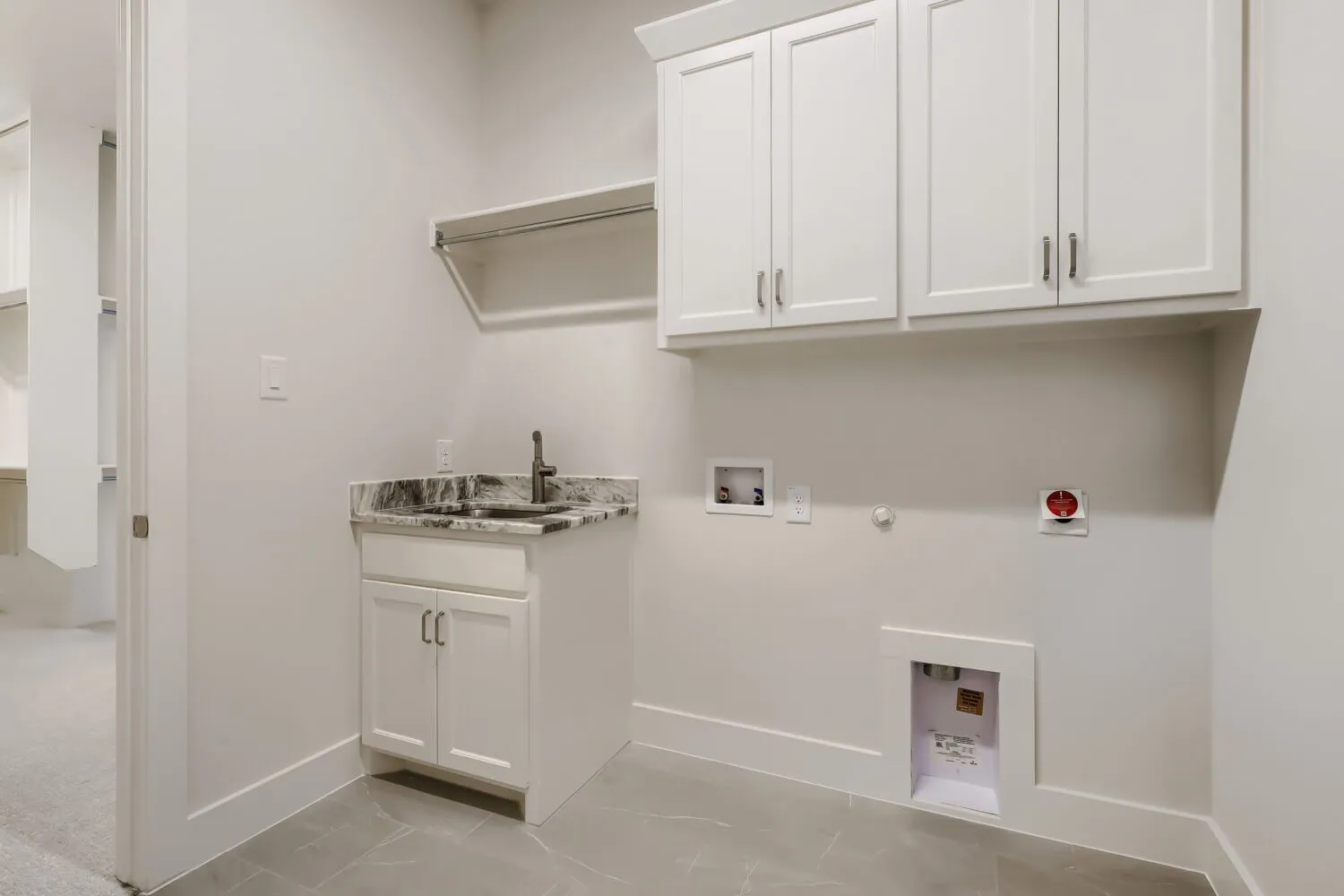 Laundry area featuring white cabinetry, a built-in sink with a dark countertop, tile flooring, and a clothes hanging rod