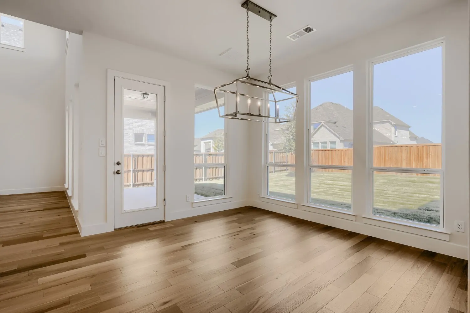 Expansive room featuring wood-finish flooring, a contemporary chandelier, multiple large windows, and a glass-paneled door