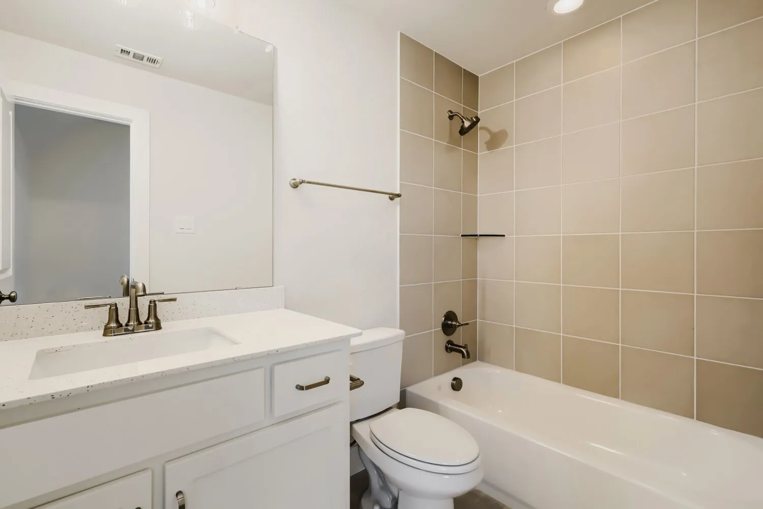 White vanity with an integrated sink and light-toned countertop, brushed nickel faucet, large wall mirror, and a tiled shower/tub combination with dark bronze fixtures