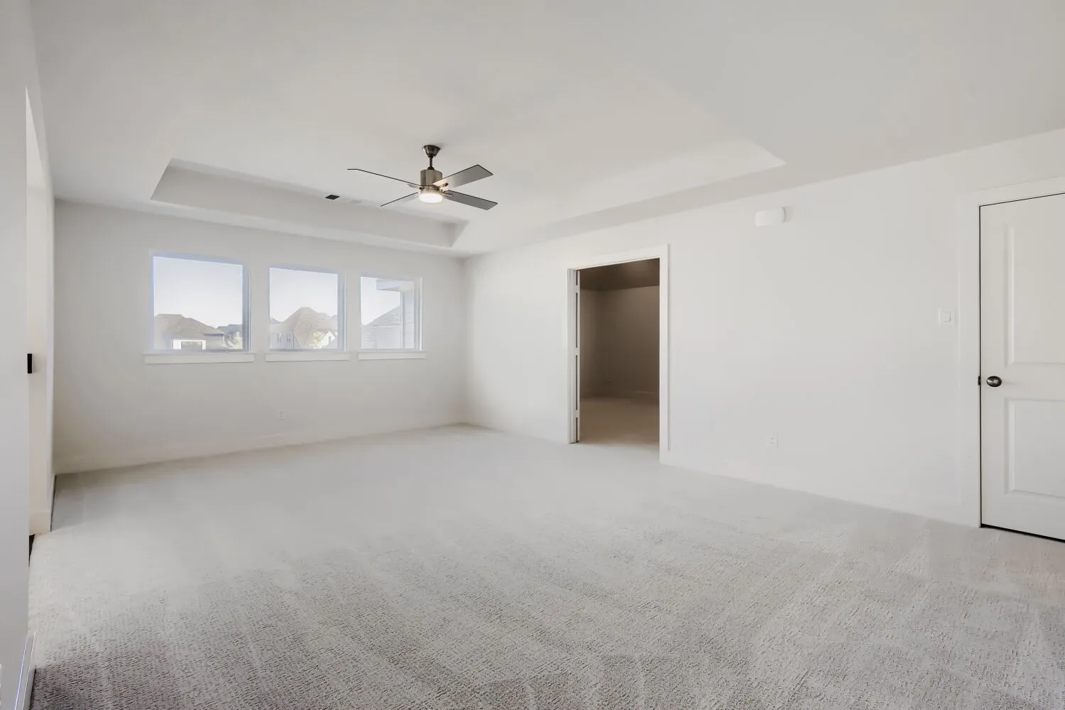 Recessed tray ceiling with a ceiling fan, three windows, and light-toned carpeting
