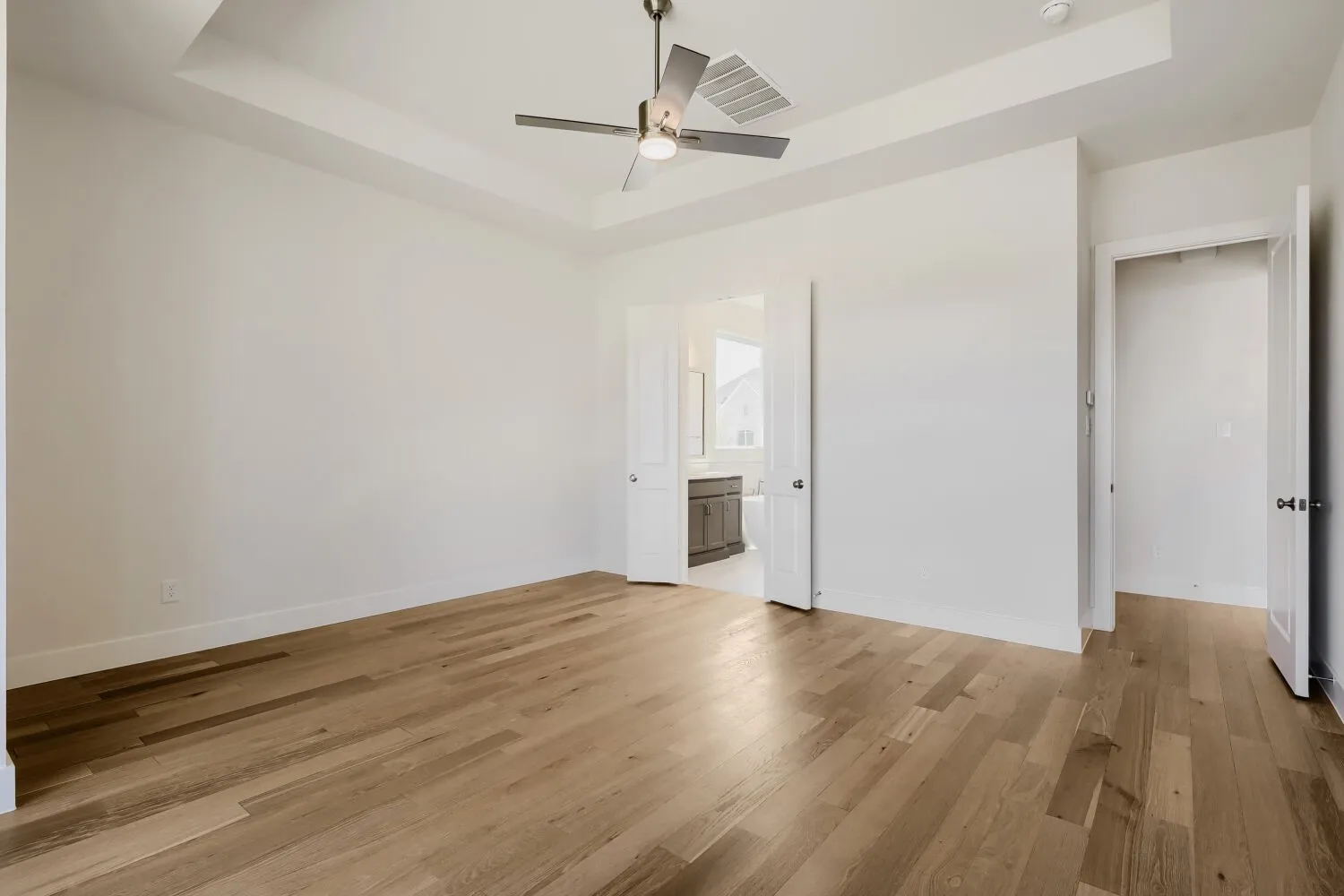 Tray ceiling with a ceiling fan, wood-finish flooring, and white walls