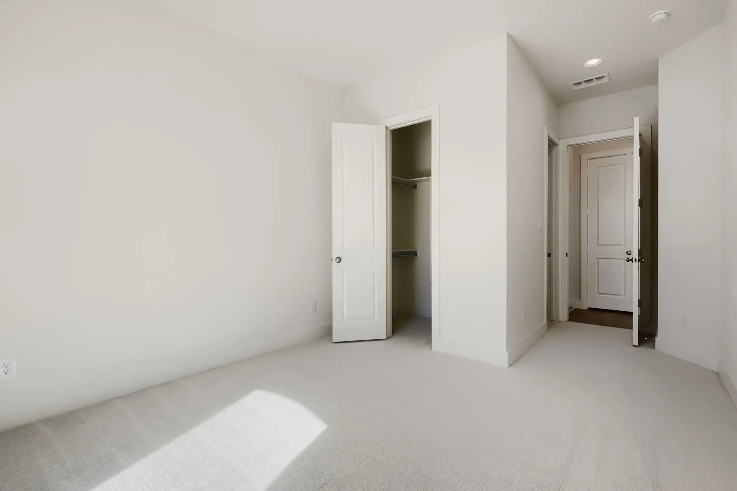 Bright, light-filled bedroom with neutral carpeting, dual closets with white bifold doors, and recessed ceiling lighting