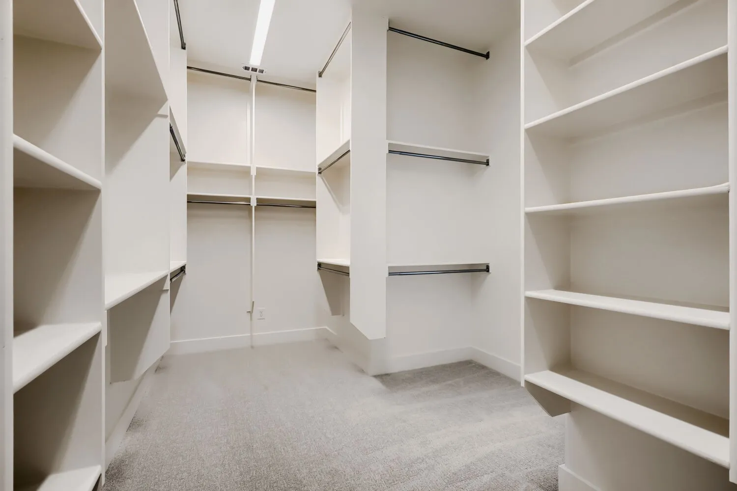 Expansive walk-in closet featuring extensive built-in shelving, multiple hanging rods, and light gray carpeting