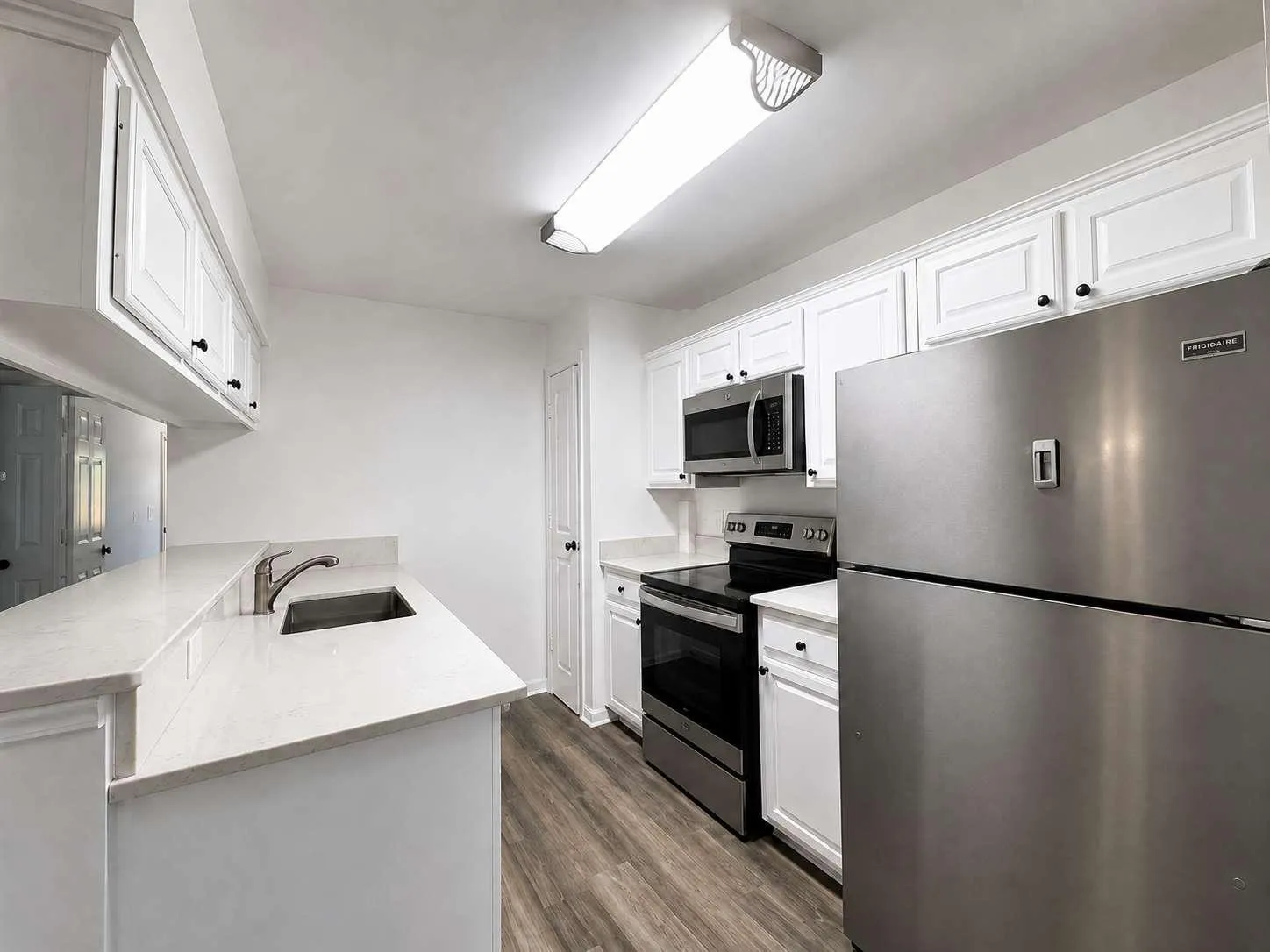 Kitchen featuring white cabinetry, stainless steel appliances, light-toned countertops, an undermount sink with a gooseneck faucet, and hard-surface flooring