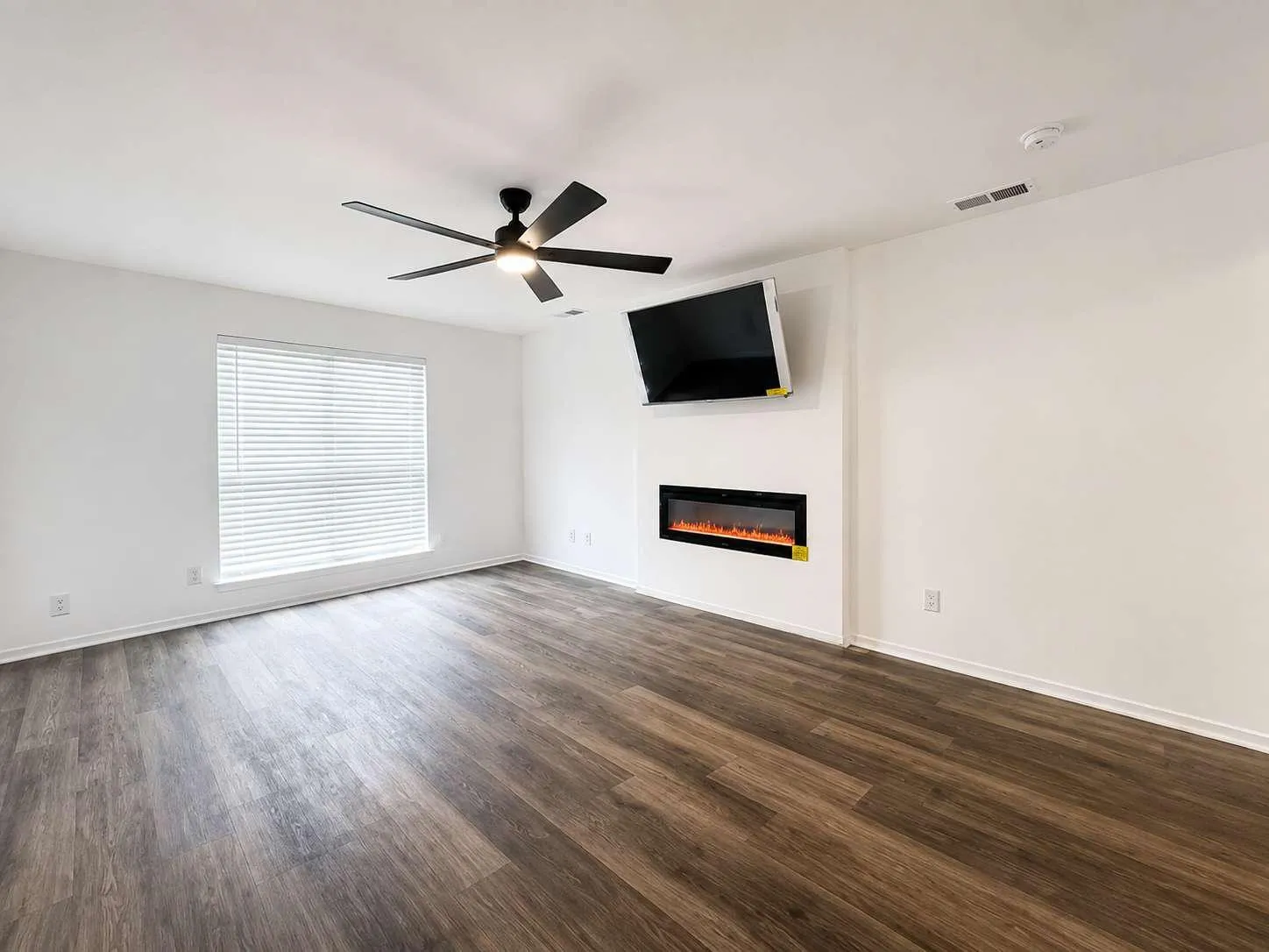 Spacious room featuring wood-finish flooring, a contemporary ceiling fan, and an integrated linear electric fireplace