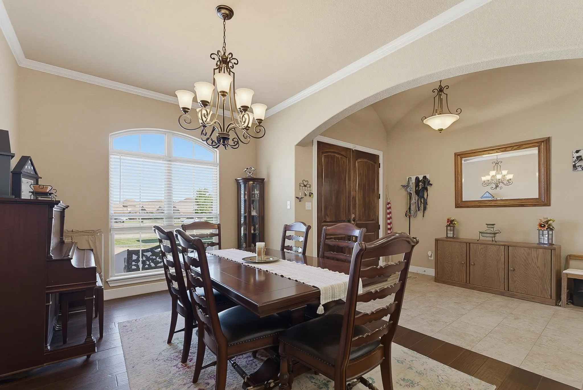 Dining area featuring dark wood-finish flooring, an arched window with blinds, and an ornate chandelier