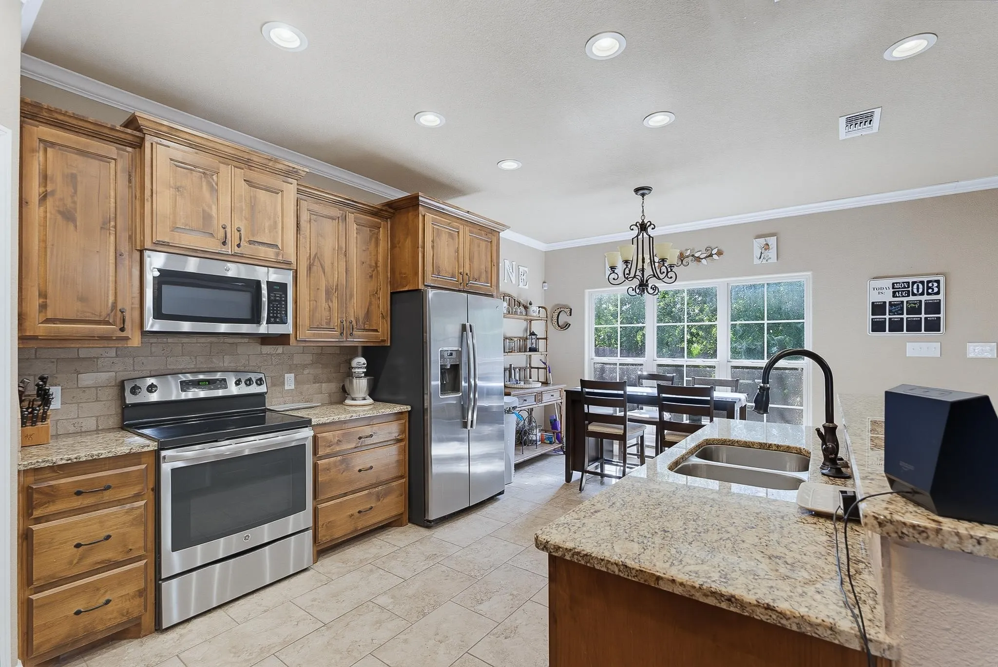 Contemporary kitchen featuring stainless steel appliances, granite countertops, wood-finish cabinetry, tile flooring, and recessed lighting