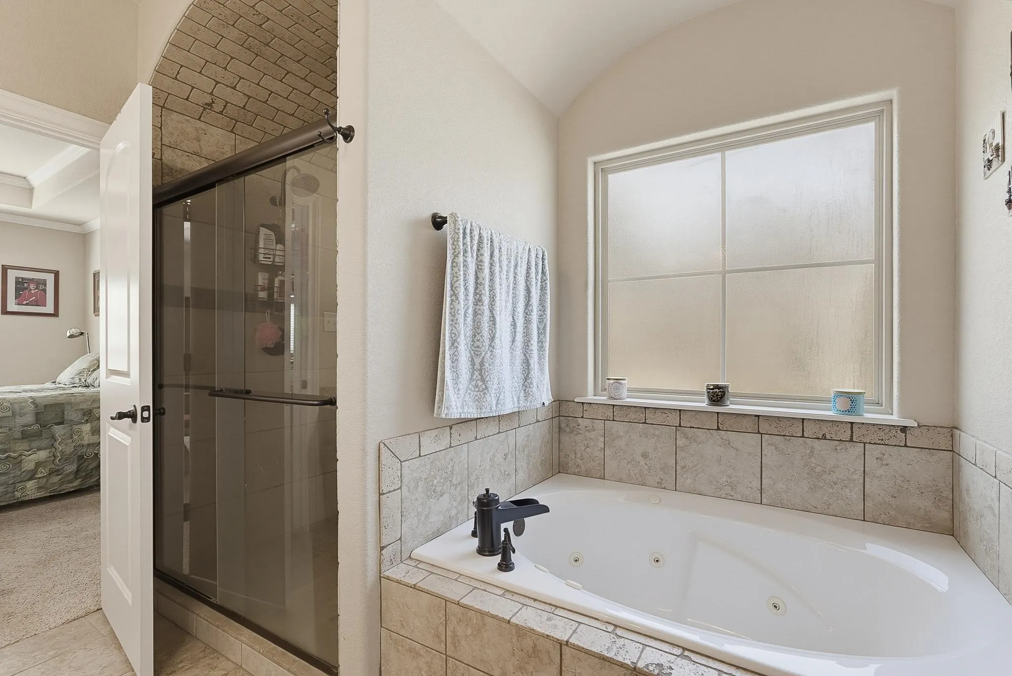 Built-in jetted tub surrounded by tile, featuring a frosted window and a dark bronze fixture