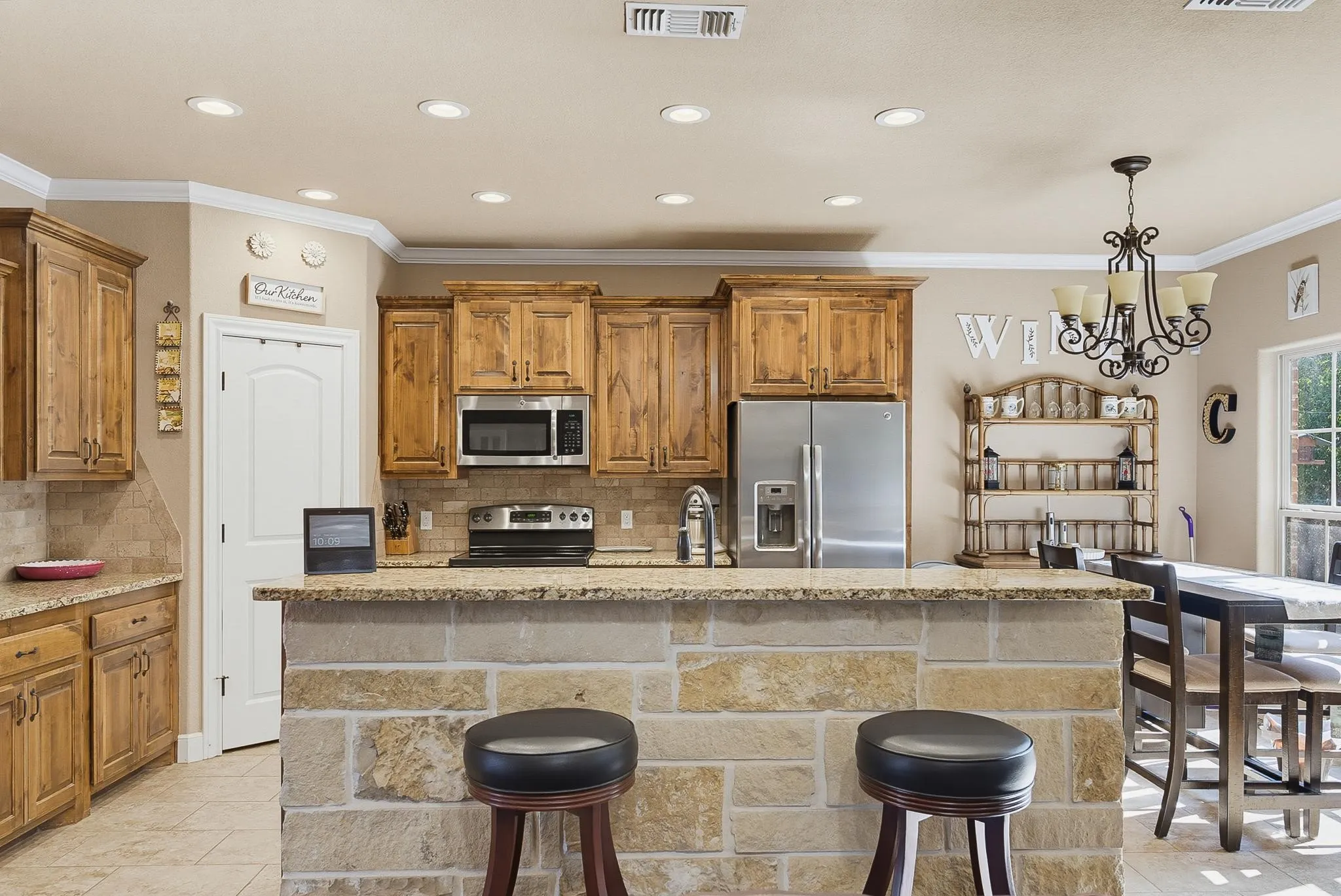 Kitchen featuring a stone-clad breakfast bar with a granite countertop, wood-finish cabinetry, stainless steel appliances, recessed lighting, and a tile backsplash